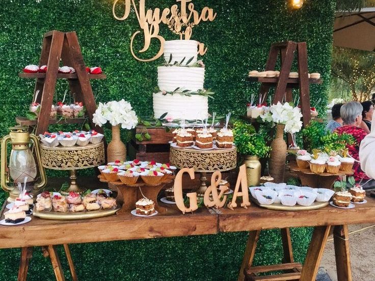 Mesa de dulces de estilo rústico con torta de novios y muro verde